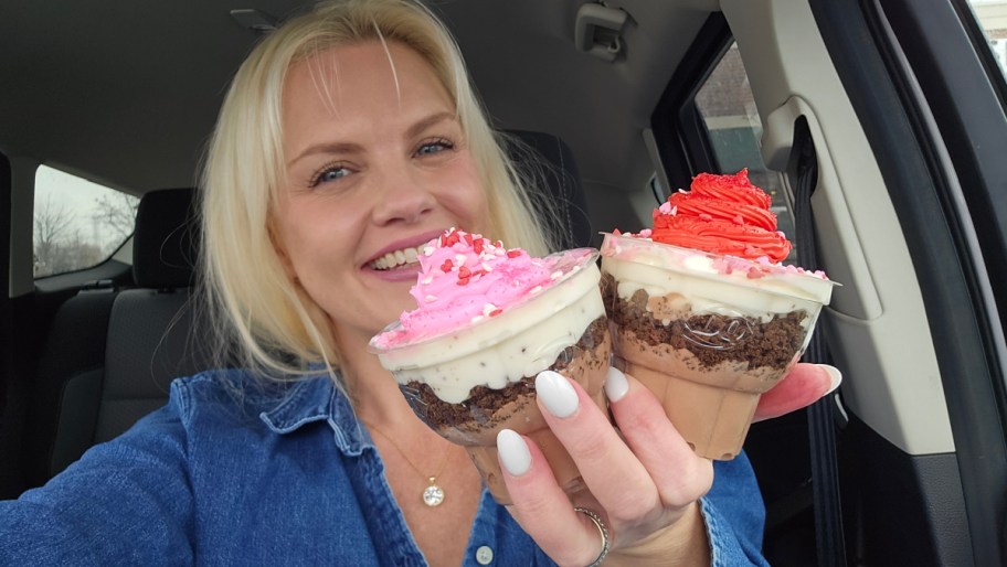 smiling woman holding two ice cream cupcakes with pink and red frosting