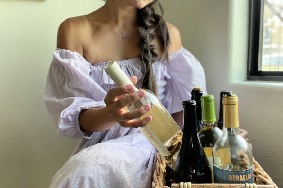 Woman in a purple dress pulling a wine bottle from a basket of wine
