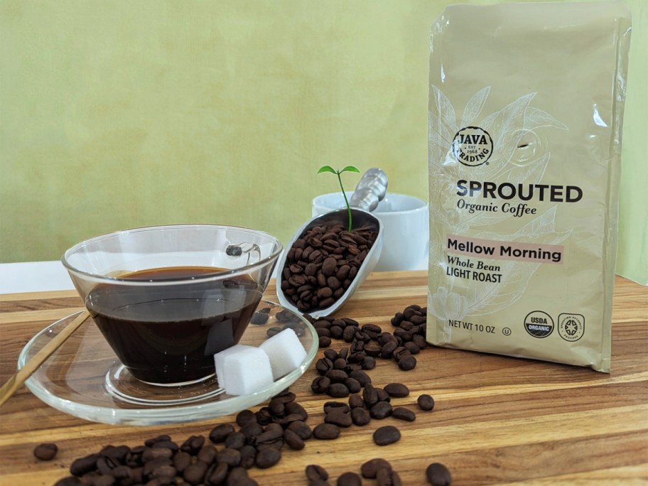 A cup of coffee next to coffee beans and a bag of coffee.