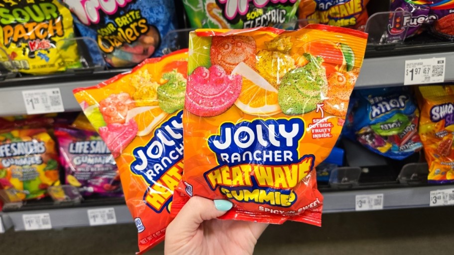 a womans hand holding 2 bags of jolly rancher heatwave gummies