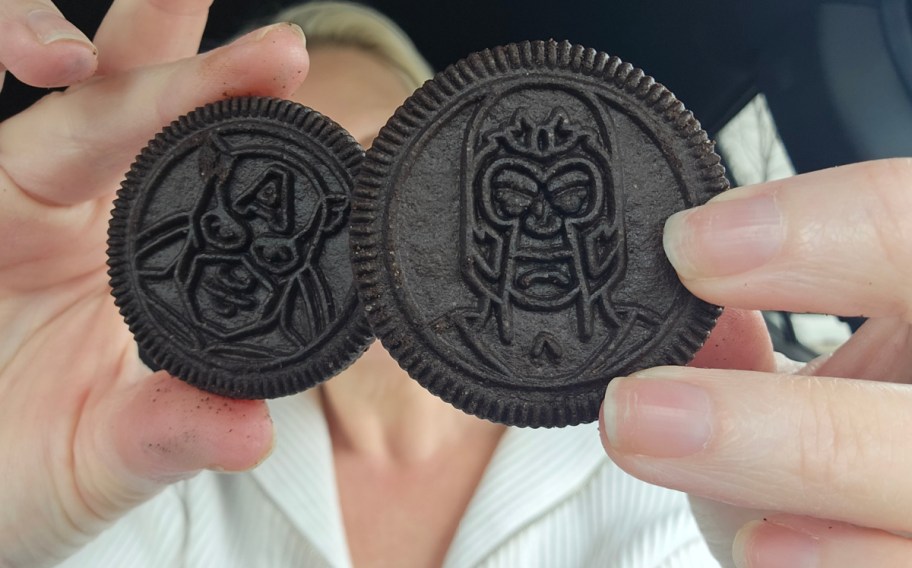 Two chocolate cookies featuring superhero designs are held close to the camera.