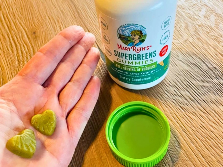 hand holding two gummies next to a bottle of Mary Ruths supergreens gummies 