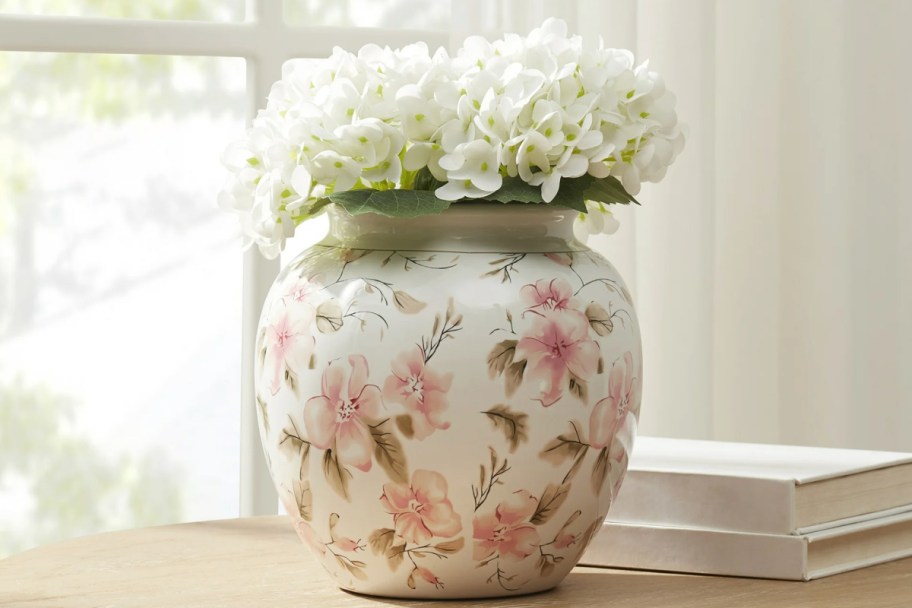 round white vase with pink flowers on it with white flowers in it