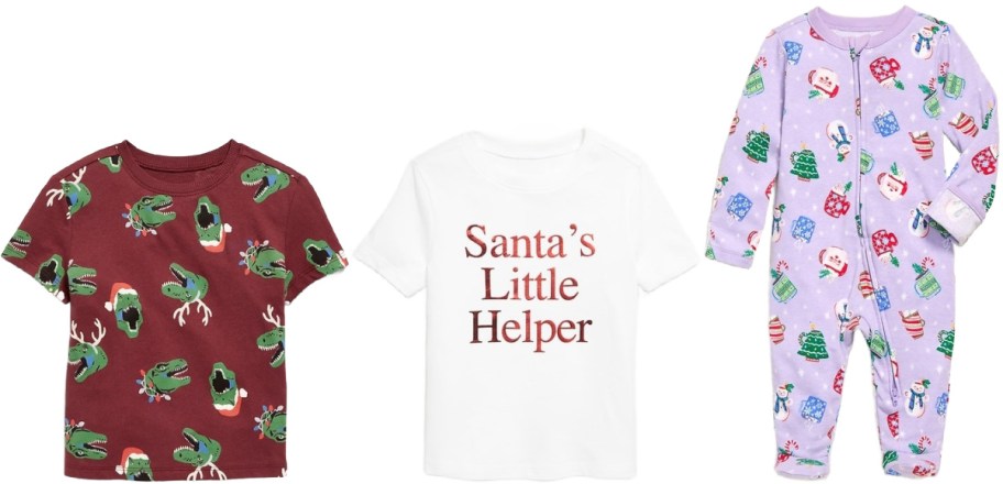 Three festive baby outfits are displayed. Left: a maroon T-shirt with green dinosaur and Santa hat pattern. Middle: white T-shirt with "Santa’s Little Helper" in red. Right: lavender onesie with holiday-themed graphics including snowflakes, gifts, and Christmas trees.