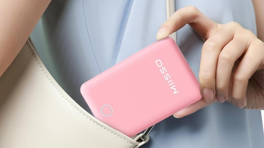 a womans hand putting a pink power bank into a shoulder bag