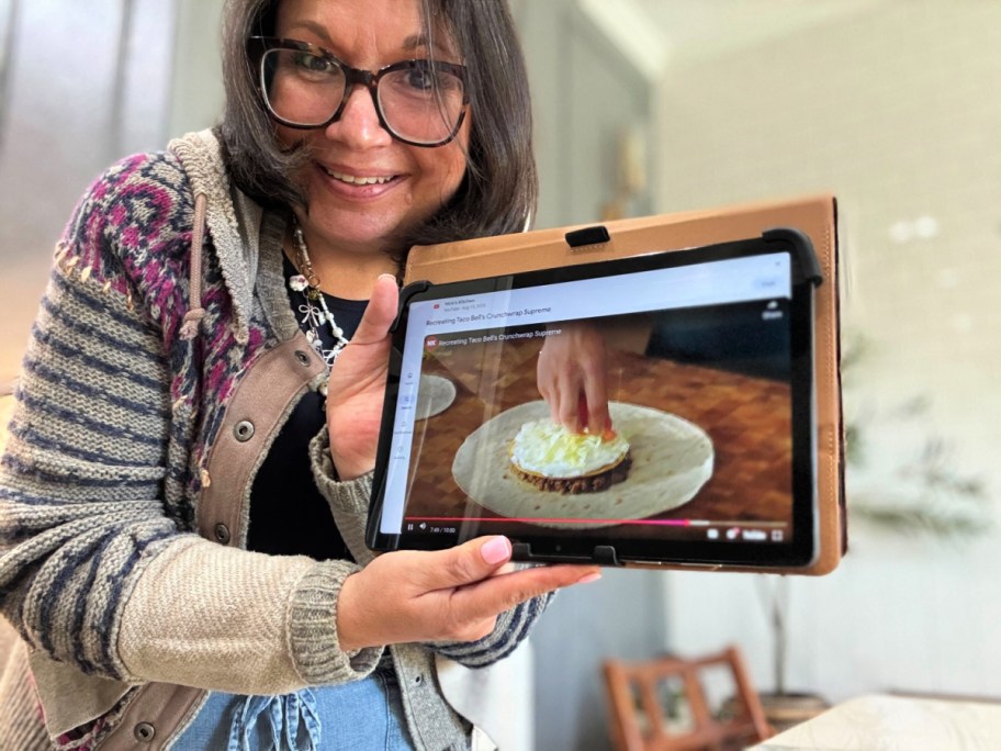 smiling woman holding a tablet showing a recipe video