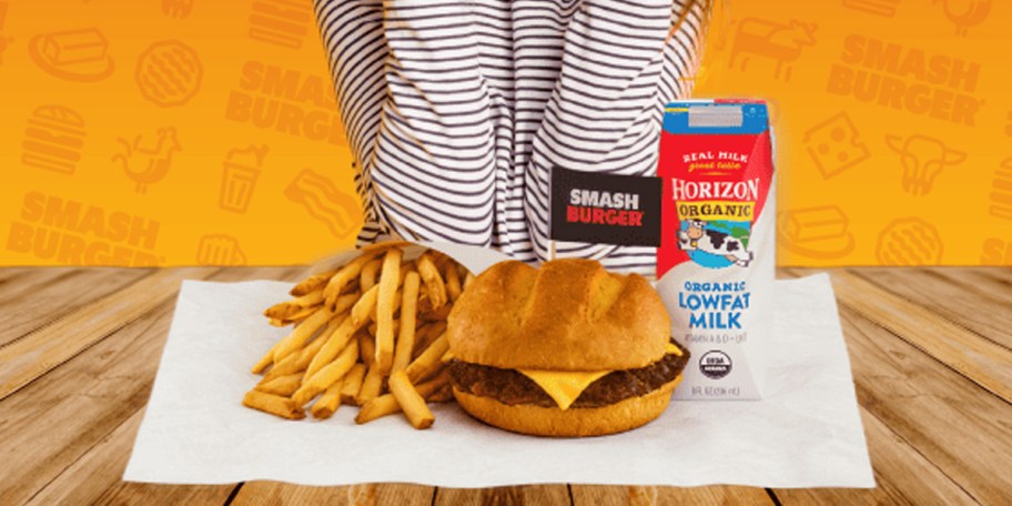 kid sitting with hamburger, fries and drink in front of them 