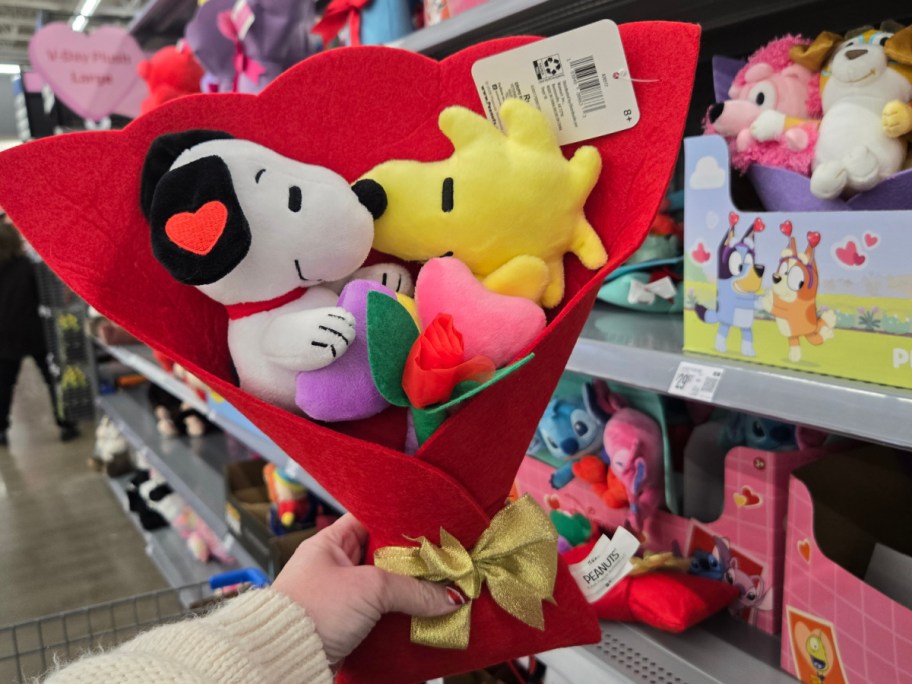 A hand holding up a Snoopy & Woodstock plush bouquet at Walmart.
