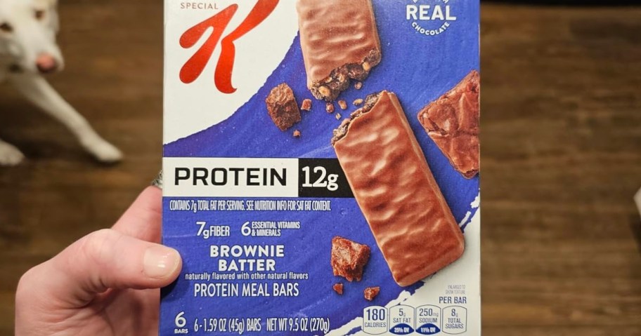 Box of Special K Brownie Batter Protein Meal Bars held in hand. The packaging shows a chocolate bar, emphasizes 12g protein and 7g fiber, with crumbs around it.