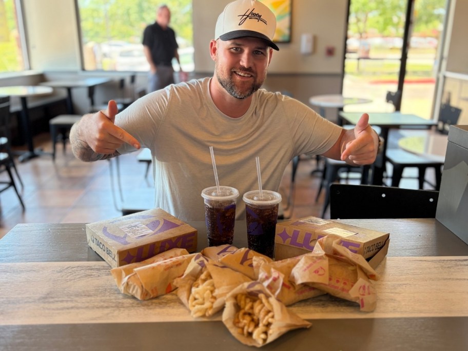 a man with two taco bell combo boxes and drinks at a table in restaurant