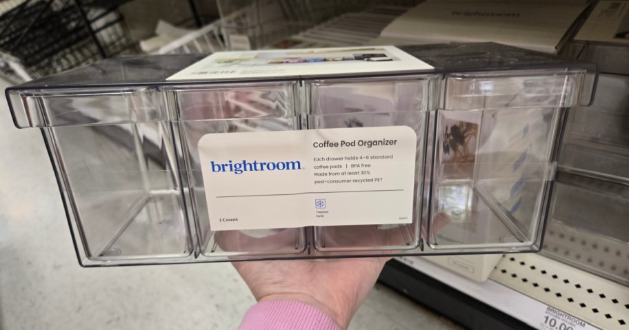 A hand holds a clear plastic coffee pod organizer with three compartments. The label reads 