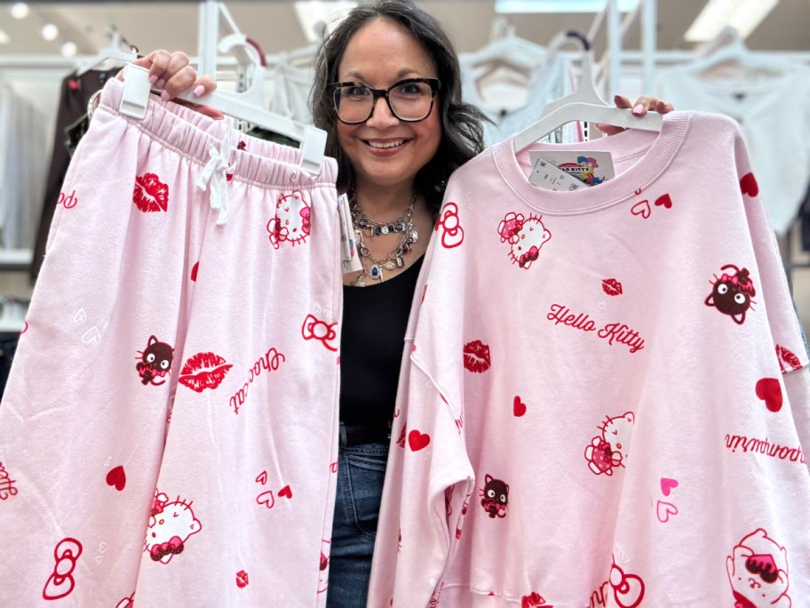 Woman smiling and holding a pink Hello Kitty fleece set with red and pink designs, including hearts and kisses.