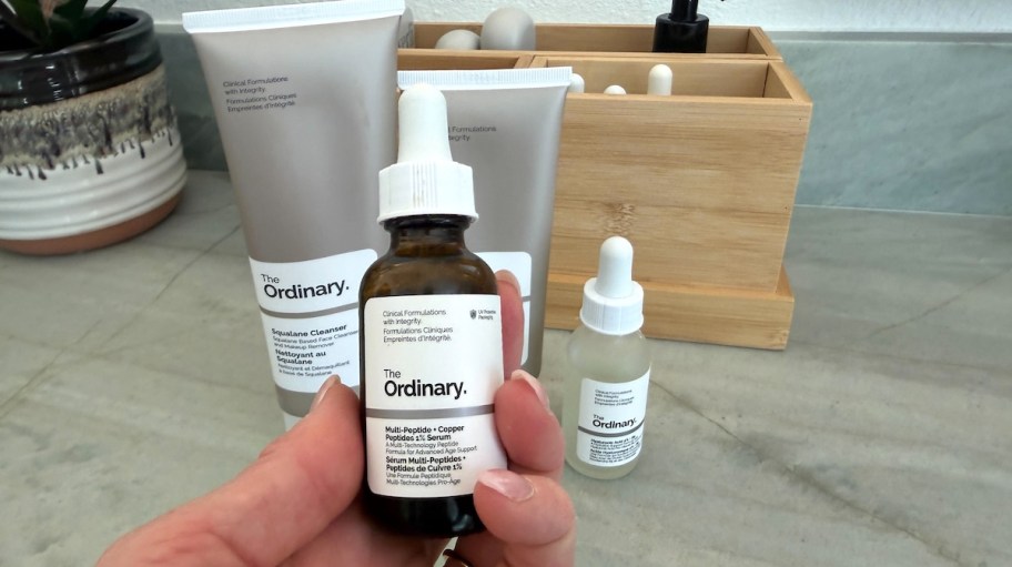hand holding a bottle of the Ordinary Skincare with more bottles behind it