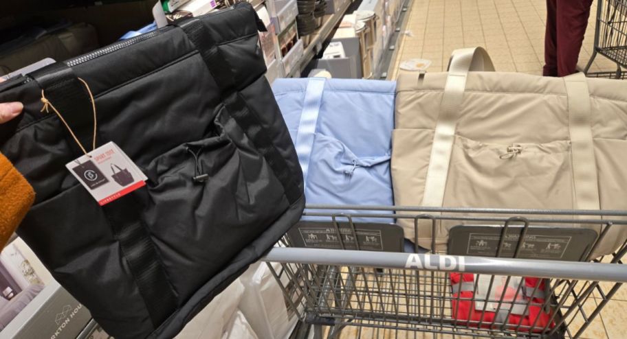 three tote bags in different colors displayed inside of shopping cart