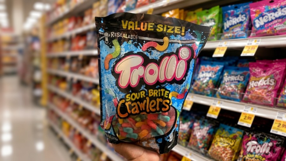 a hand holding a bag of trolli gummy candy on a store aisle