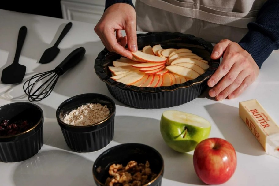 a woman placing apple slices into a ceramic pie dish
