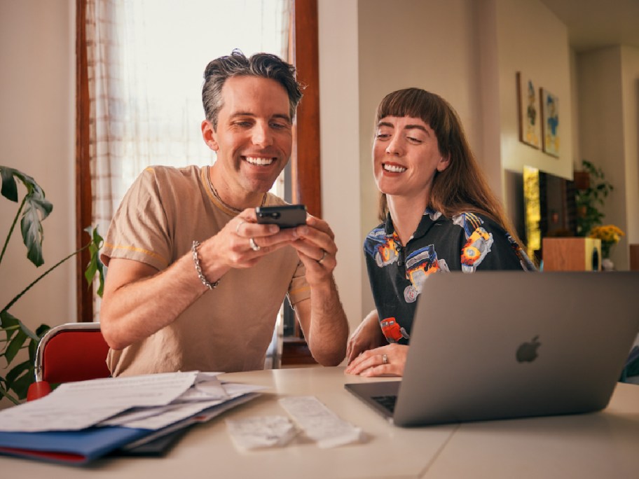 man and woman looking at a phone behind a laptop