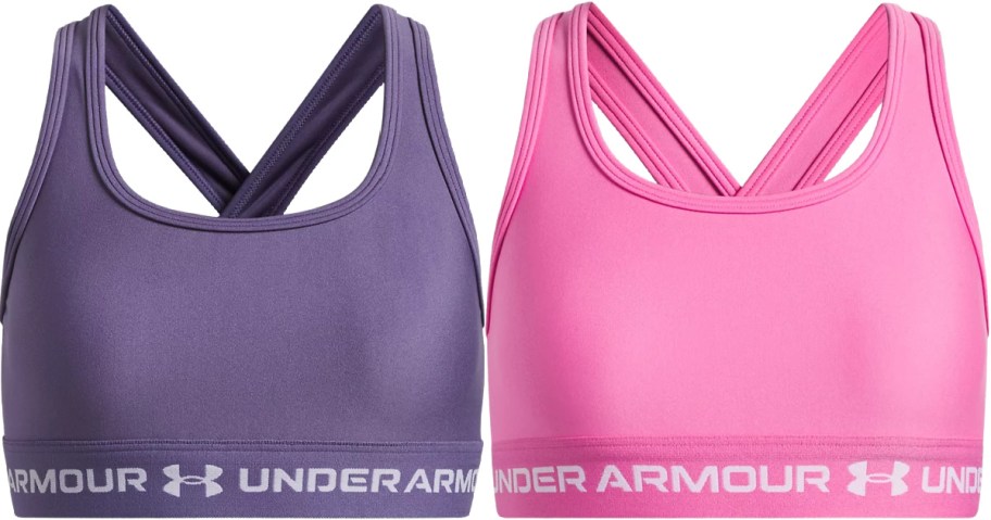 Two girls' Under Armour sports bras side-by-side: a purple cross-back bra and a pink cross-back bra.