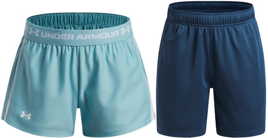 Two pairs of kids' Under Armour shorts side-by-side: a light teal pair with a branded waistband and a navy blue pair.