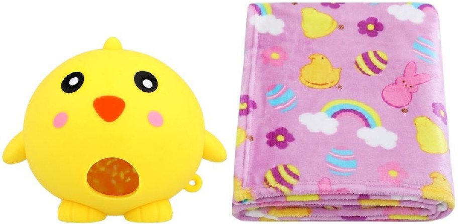 A yellow chick stress ball with a red beak sits beside a folded, pink fleece blanket. The blanket is decorated with chicks, rainbows, and eggs.