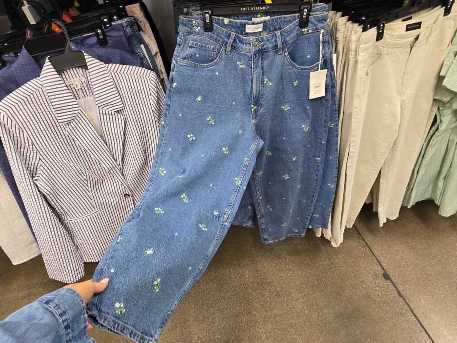 woman pulling a pair of embroidered crop jeans away from a store shelf