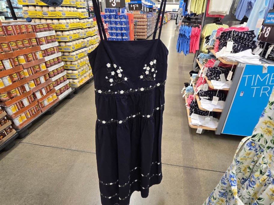 hand holding a women's black sundress with floral embroidery