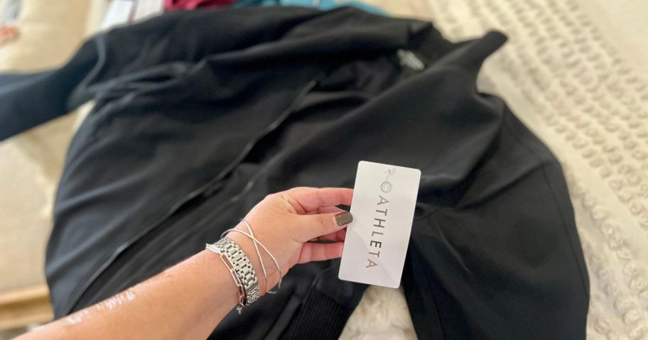 Hand holding the Athleta tag on a black jacket on a bed