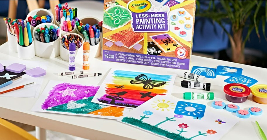 Art supplies on a table with Crayola Less-Mess Painting Activity Kit. Includes colorful markers, crayons, paint pots, and vibrant paintings.