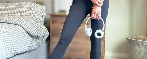 woman wearing black leggings and top and holding a pair of white headphones