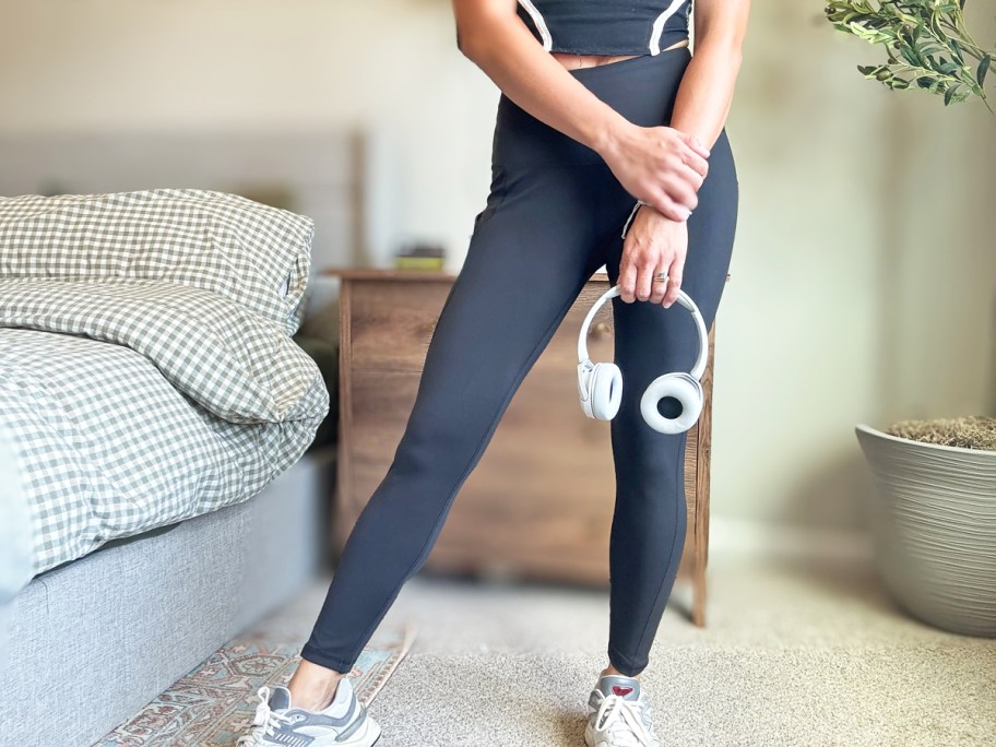 woman wearing black leggings and top and holding a pair of white headphones