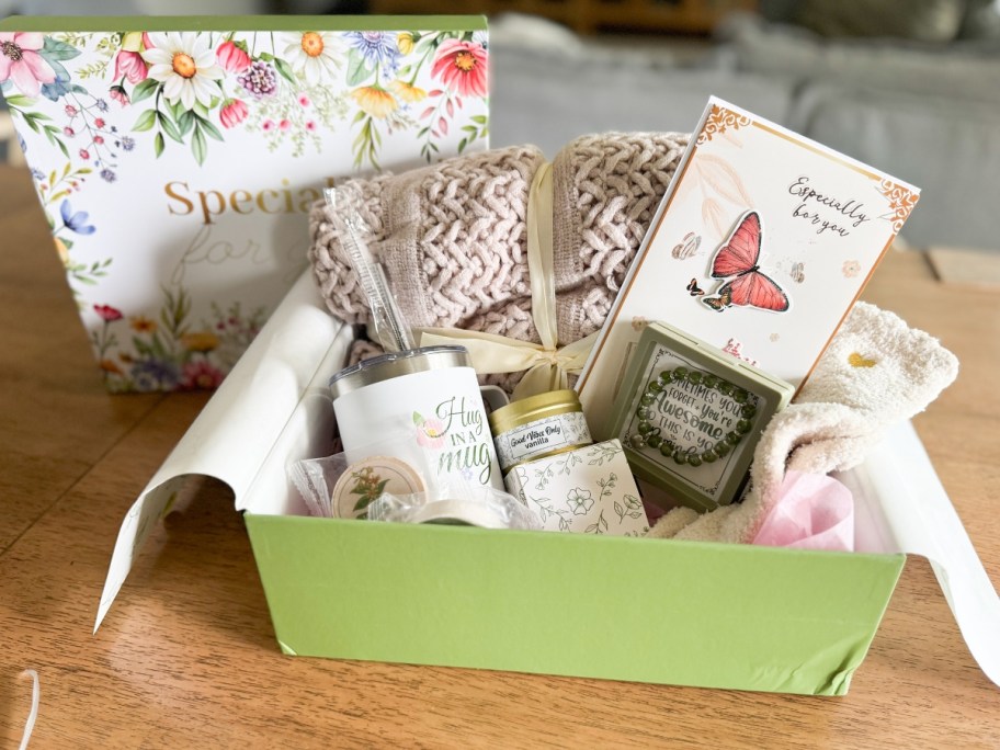 a gift box with a blanket, mug, candle, socks, and card 