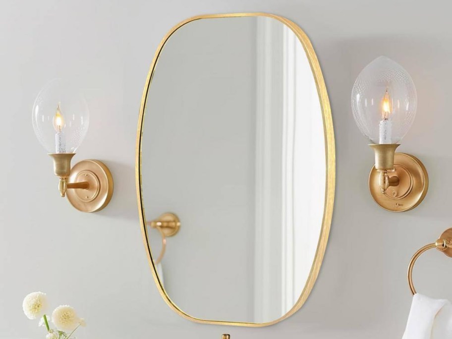 LuxHomez Oval Aluminum Frame Wall Mirror in gold hanging on wall between two sconces
