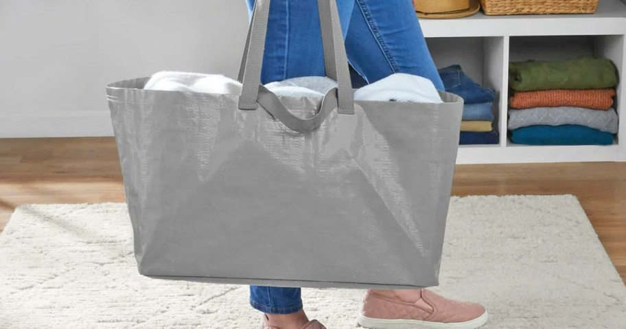 woman holding a large grey tote bag with bedding inside