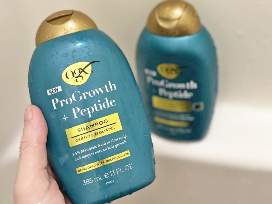 hand holding a teal bottle of OGX ProGrowth + Peptide Clarifying Shampoo in shower