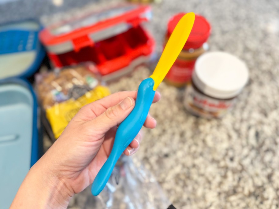 hand holding teal and yellow OTOTO Splatypus Jar Spatula