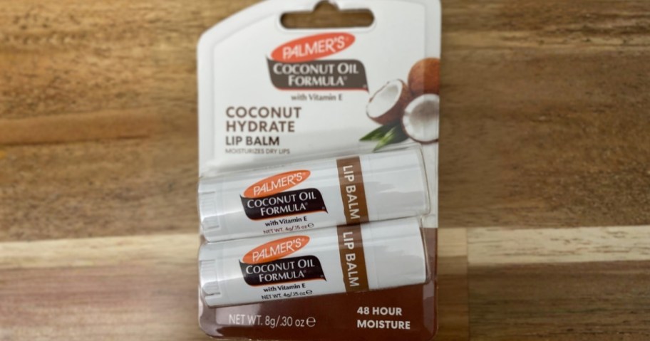 two sticks of palmer's coconut oil lip balm in packaging on wood floor