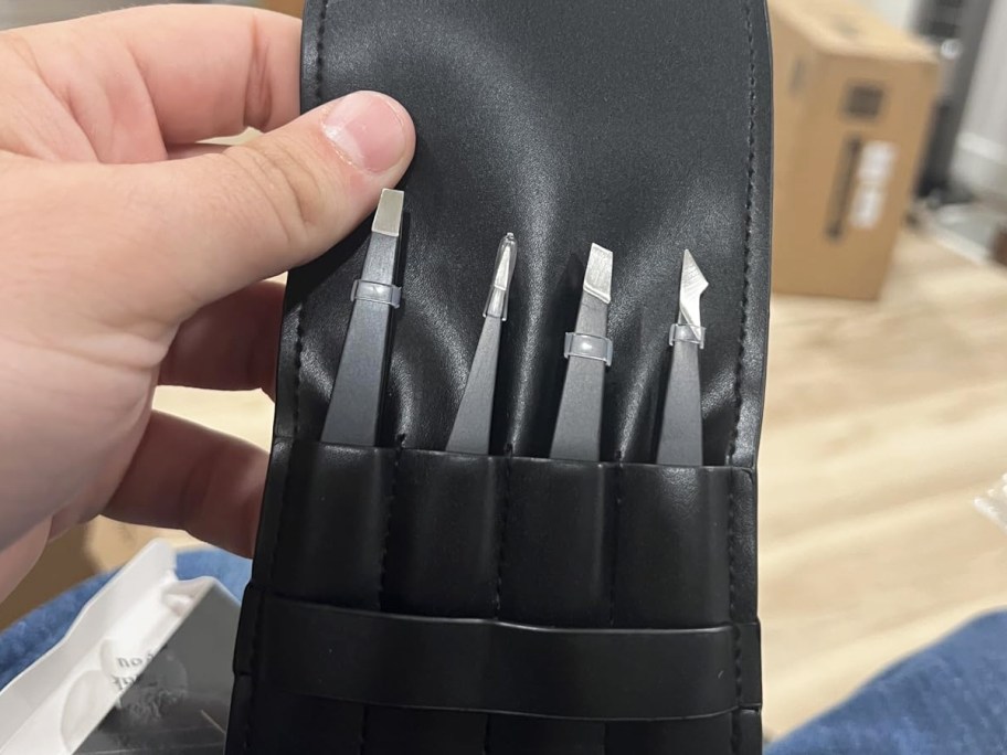 hand holding up a set of tweezers in a black leather storage case