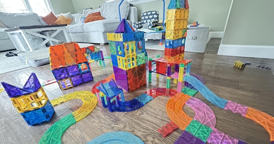 A large and colorful magnetic tile castle and race track set built on a hardwood floor in a living room.