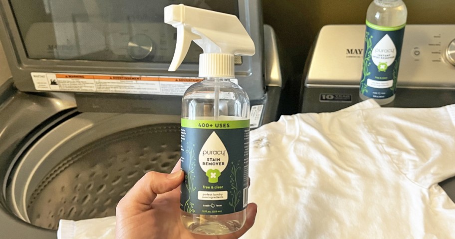 hand holding bottle of Puracy Stain Remover with white shirt and washing machine in background