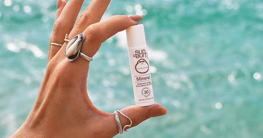 hand holding up white tube of Sun Bum Lip Balm