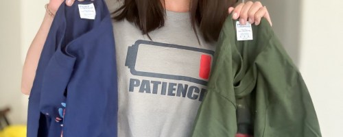 woman wearing tee with low battery patience graphic on front holding two t-shirts