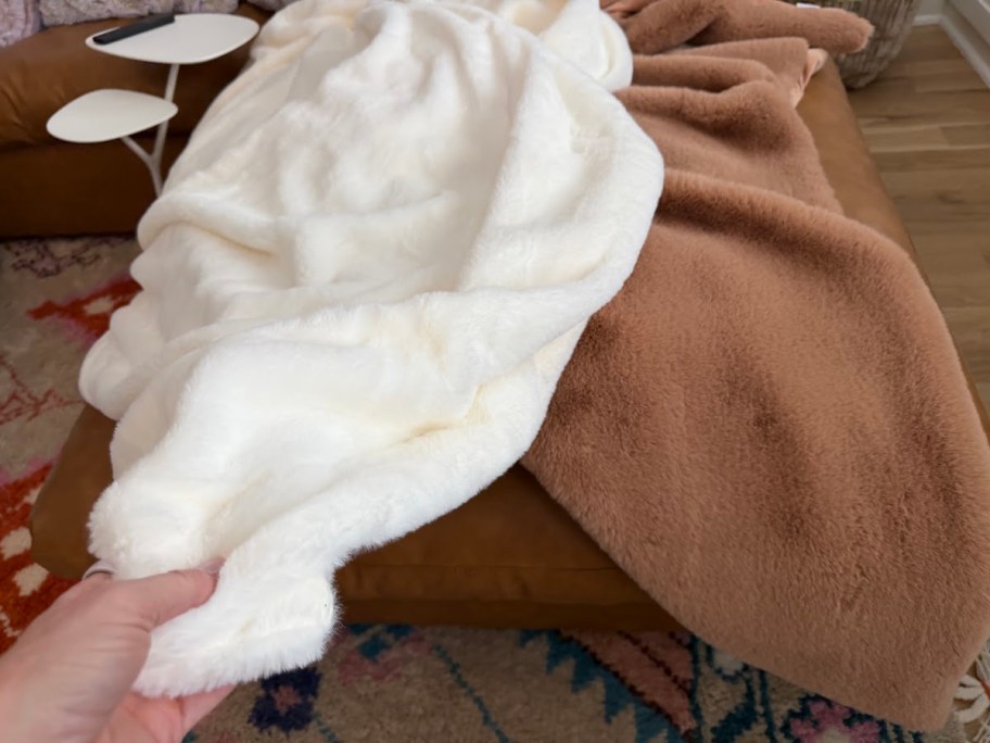 hand holding white faux fur throw blanket on couch next to brown blanket