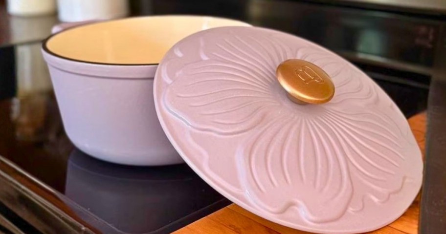 a pink dutch oven with a lid with floral details on a stove