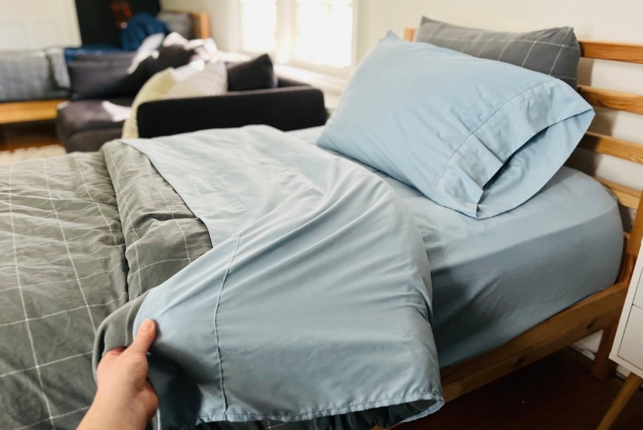 womans hand holding the corner of a blue flat sheet