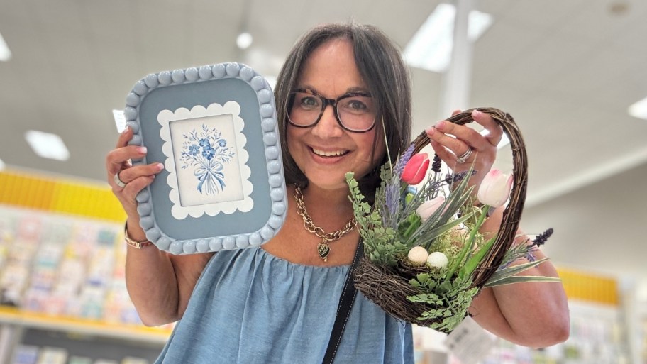 a woman holding a picture frame and an artificial floral arrangement