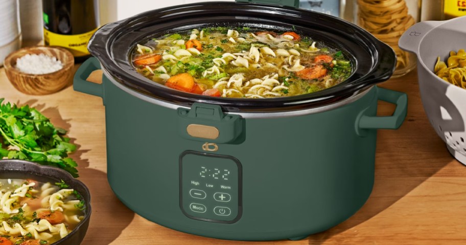 dark green slow cooker with food inside on table