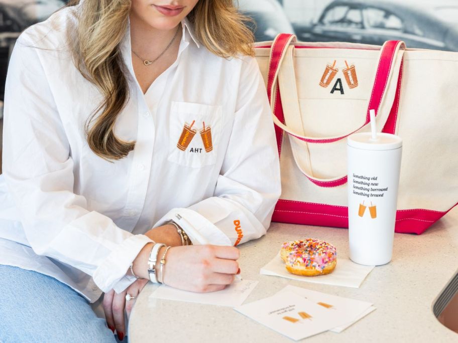 woman wearing dunkin' "something brewed" shirt next to other merchandise