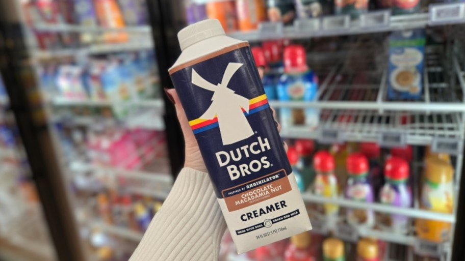 a womans hand holding a container of dutch bros creamer in front of a dairy case