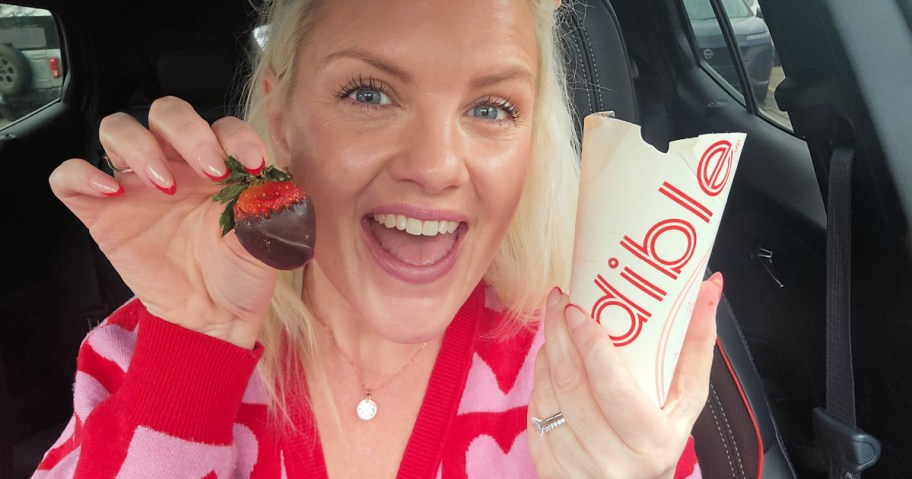 woman holding up a chocolate covered strawberry in her car