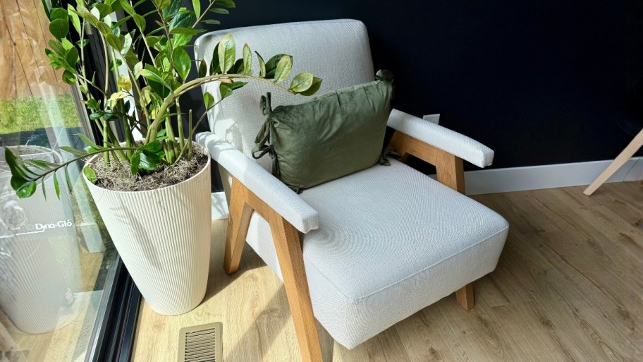 a white accent chair with a green pillow sitting next to a plant